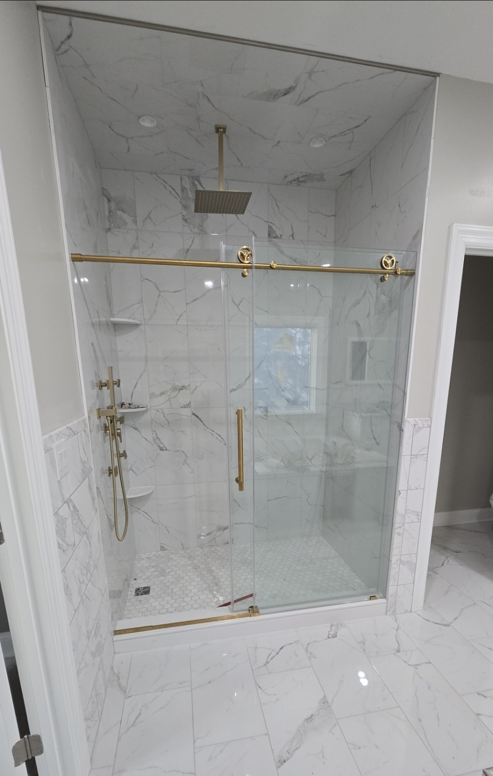 Marble-look tiled shower with glass doors and brushed gold fixtures