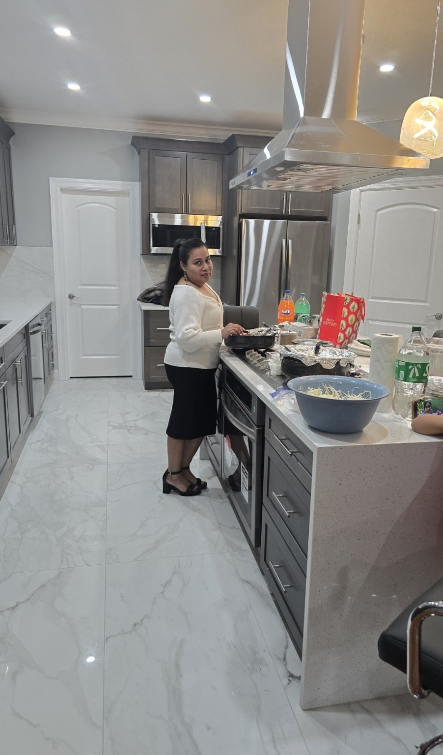 Modern kitchen with gray cabinetry, marble-look flooring, and a stainless steel island range hood